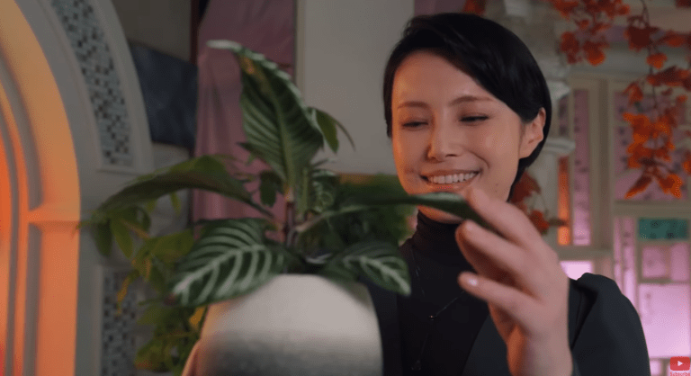 The Lady smiling while touching a plant in her garden space in Kamen Rider Zeztz Episode 16