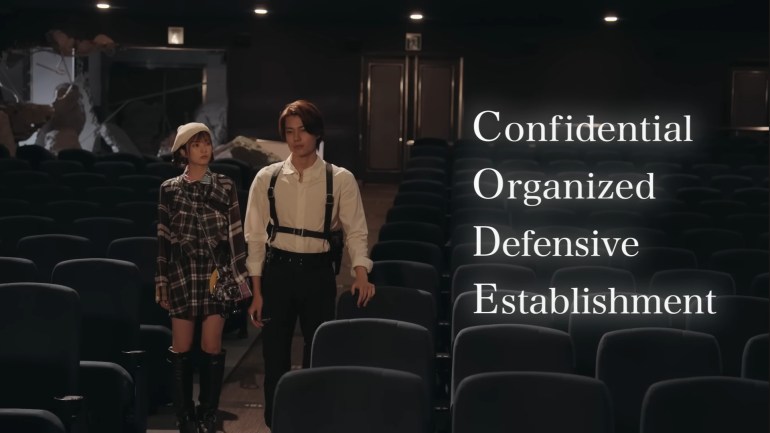 Baku Yorozu and Nem walking through an abandoned theater as the acronym CODE appears on screen meaning Confidential Organized Defensive Establishment in Kamen Rider Zeztz Episode 26.