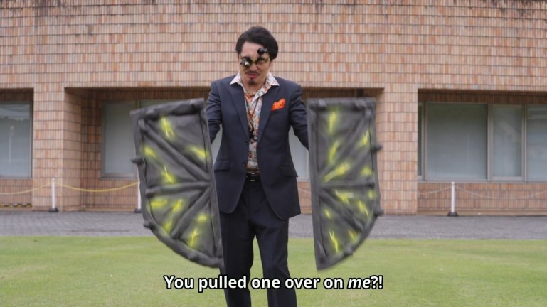 A con artist wearing oversized novelty glasses projects two massive glowing shields while confronting Shout.