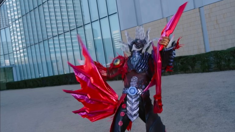 Oblivion holds a large red wing torn from Kamen Rider Zeztz during their outdoor battle.