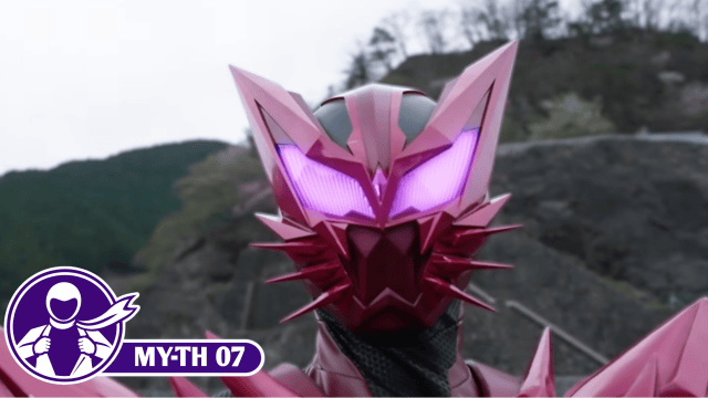 Close-up of Kamen Rider Maou's angular pink-and-red helmet, featuring glowing purple eyes, tall pointed ears, and sharp spikes around the mouth. A purple MY-TH 07 graphic appears in the lower-left corner.