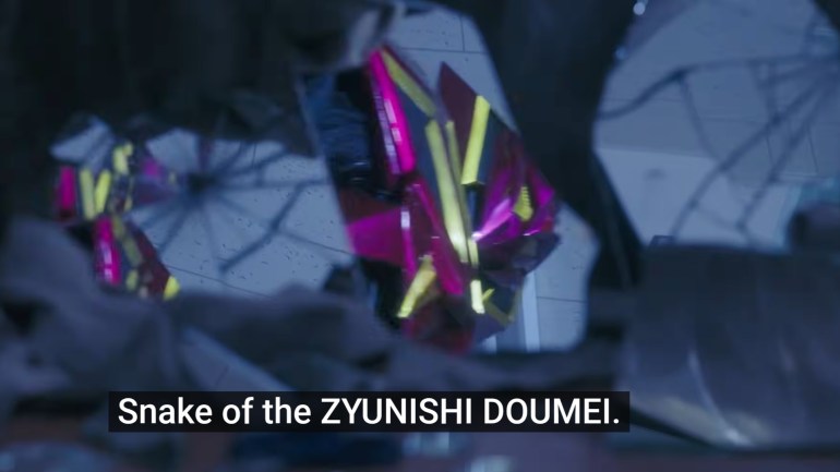 Jyao’s magenta and yellow helmet reflected in broken glass, with subtitles reading, “Snake of the ZYUNISHI DOUMEI.”